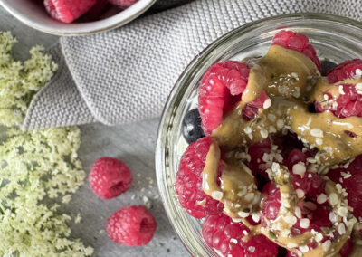 Detailaufnahme des Toppings: Frische Himbeeren und Blaubeeren, dekorativ angerichtet in einem Glas mit Overnight Oats, verfeinert mit nussigem Pistazienmus und einem Hauch Hanfsamen – ein nährstoffreiches, liebevoll zubereitetes Frühstück.