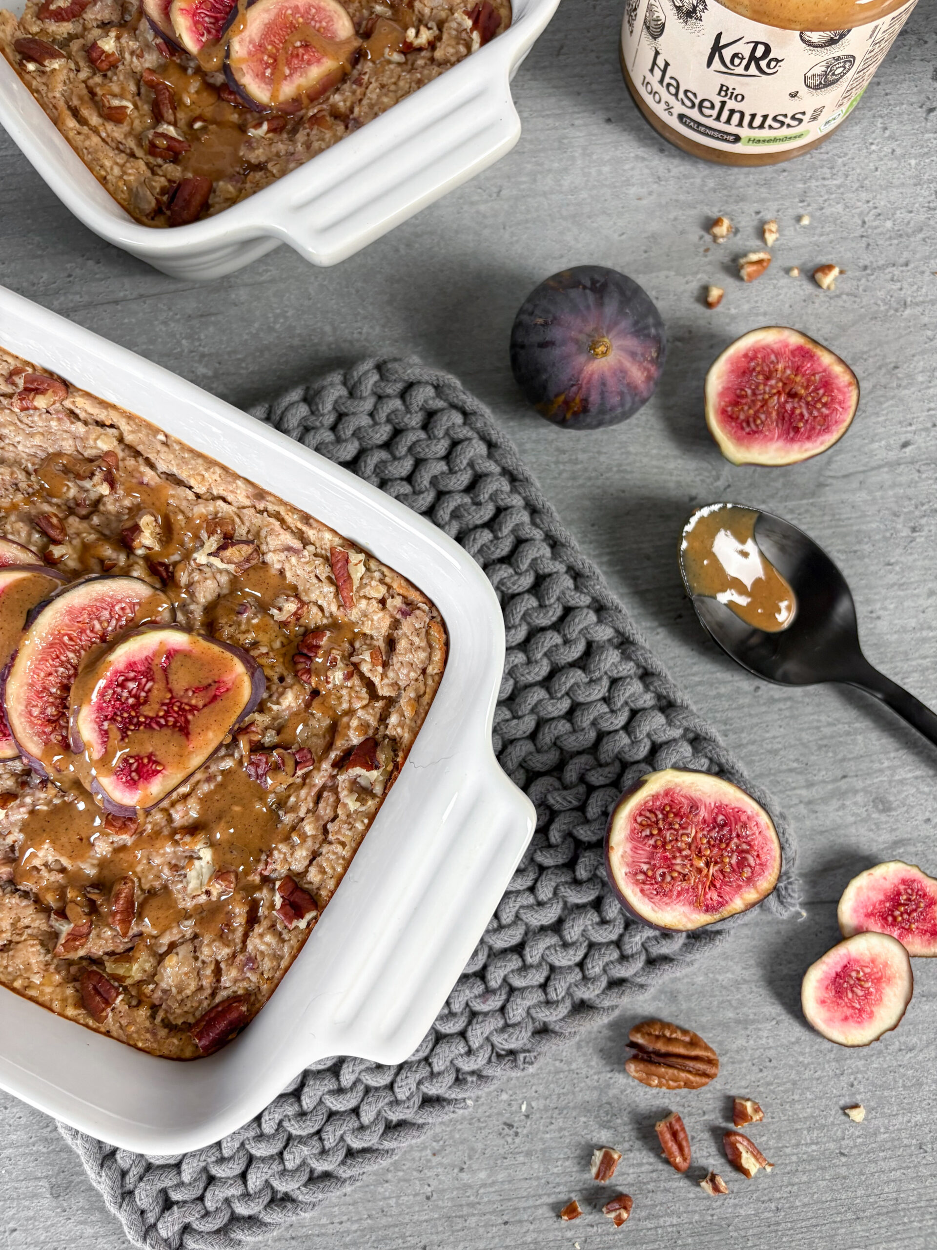Protein Baked Oats mit Feigen und Zimt – cremig gebacken, mit Pekannüssen und frischen Feigen auf grauem Holzuntergrund. Ein gesundes, eiweißreiches Frühstücksrezept für den Herbst.